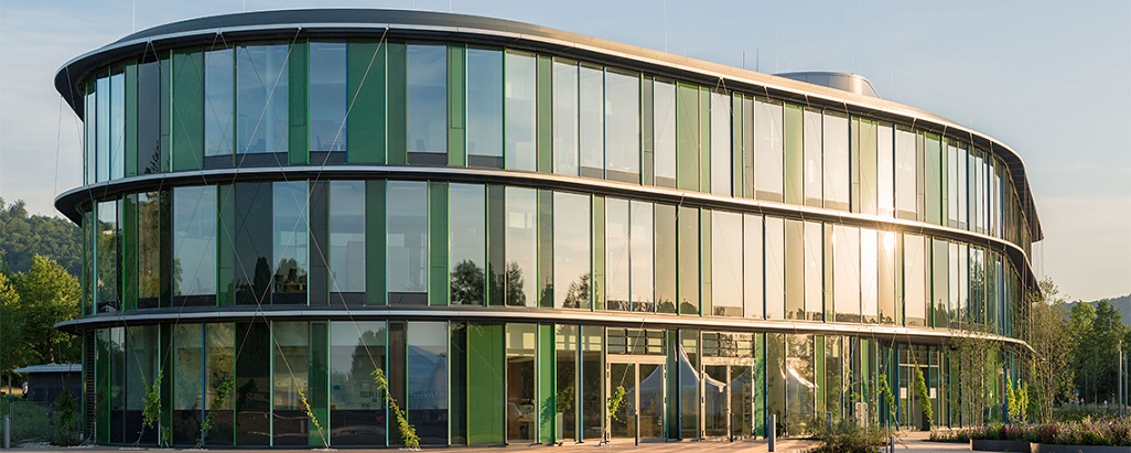 Modernes Firmengebäude der WALA Heilmittel GmbH mit markanter Wabenstruktur. Die Fassade besteht aus sechseckigen Elementen, die an eine Bienenwabe erinnern, und ist von viel Grün umgeben. Das architektonische Design verbindet Natur und Innovation